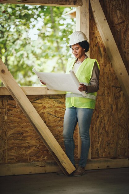 shot african female architect checking plans construction site new wooden house she is wearing protective workwear white helmet 360066 21349.jpg