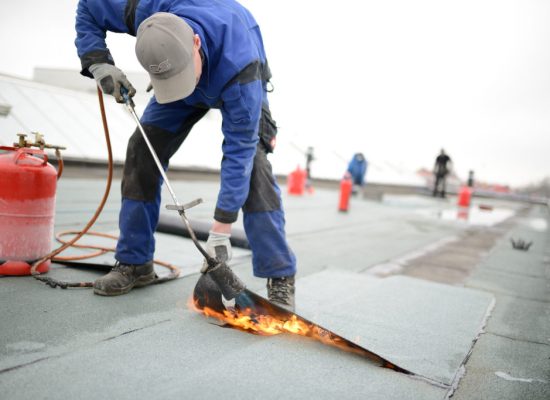 flachdach reparatur: dachdecker verschweißt dachabdichtung. dachsanierung mit gasbrenner. immer feuerlöscher vorhalten.